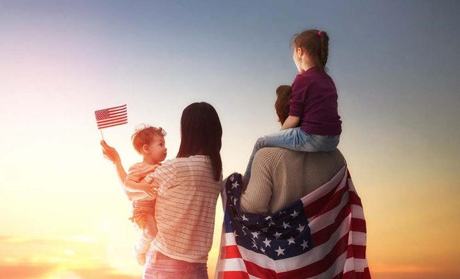 Patriotic holiday. Happy family, parents and daughters children girls with American flag outdoors. USA celebrate 4th of July.